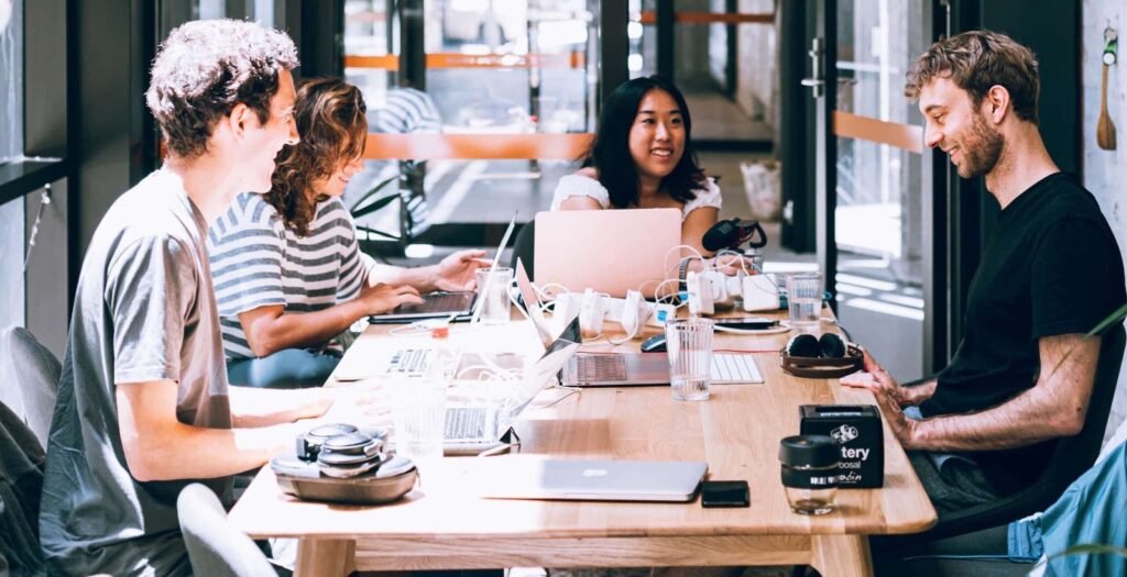 Time trabalhando em mesa compartilhada de coworking, com notebooks e conversa em andamento