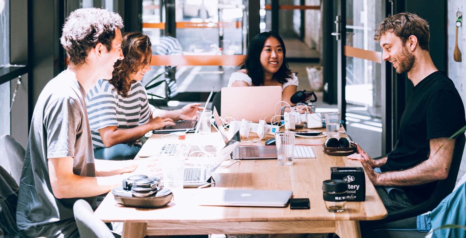 Time trabalhando em mesa compartilhada de coworking, com notebooks e conversa em andamento